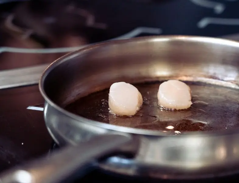 Noix de Saint-Jacques dorées dans une poêle, jus rendu au fond, persil et beurre